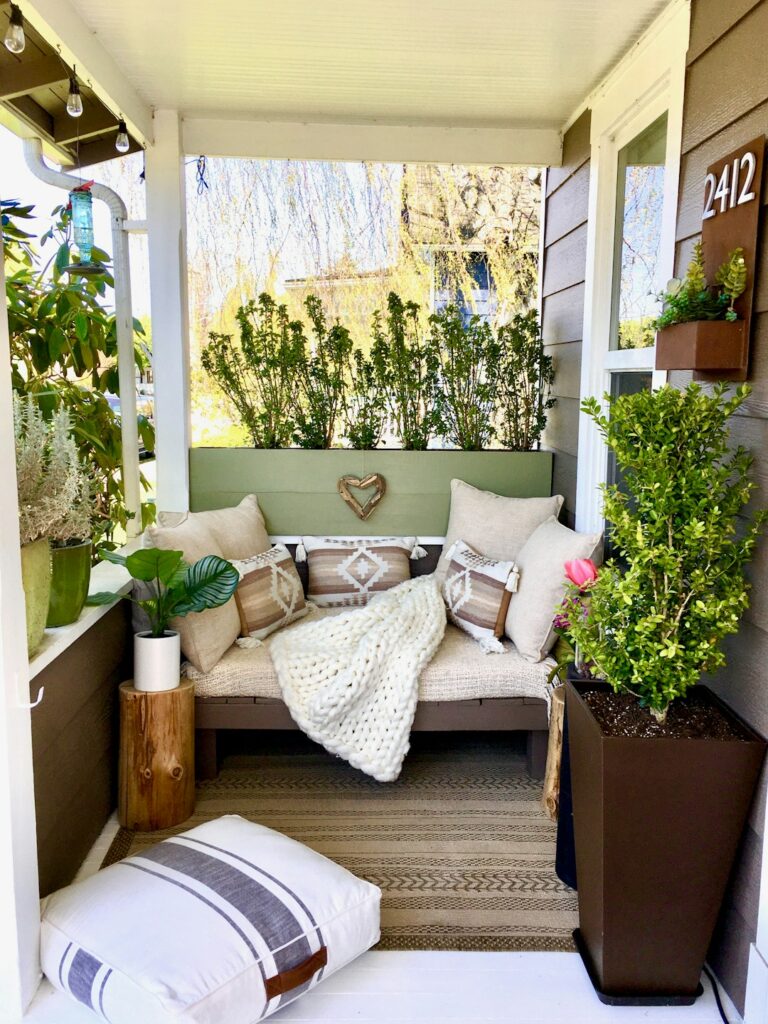 A small patio with compact seating, potted plants, and string lights above a tidy outdoor rug.